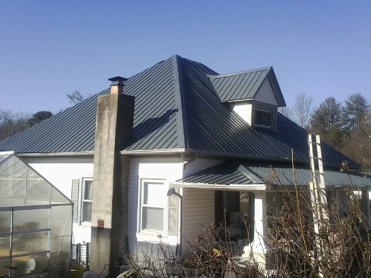 Dark blue standing seam metal roof on a white farmhouse with dormer — Slate & Tile Roof Repair by Roofing Brothers in Universal City