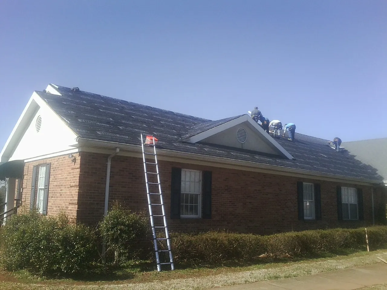 Crew tearing shingles off a brick ranch roof with a ladder set — Emergency Roof Repair work by our crew in Universal City