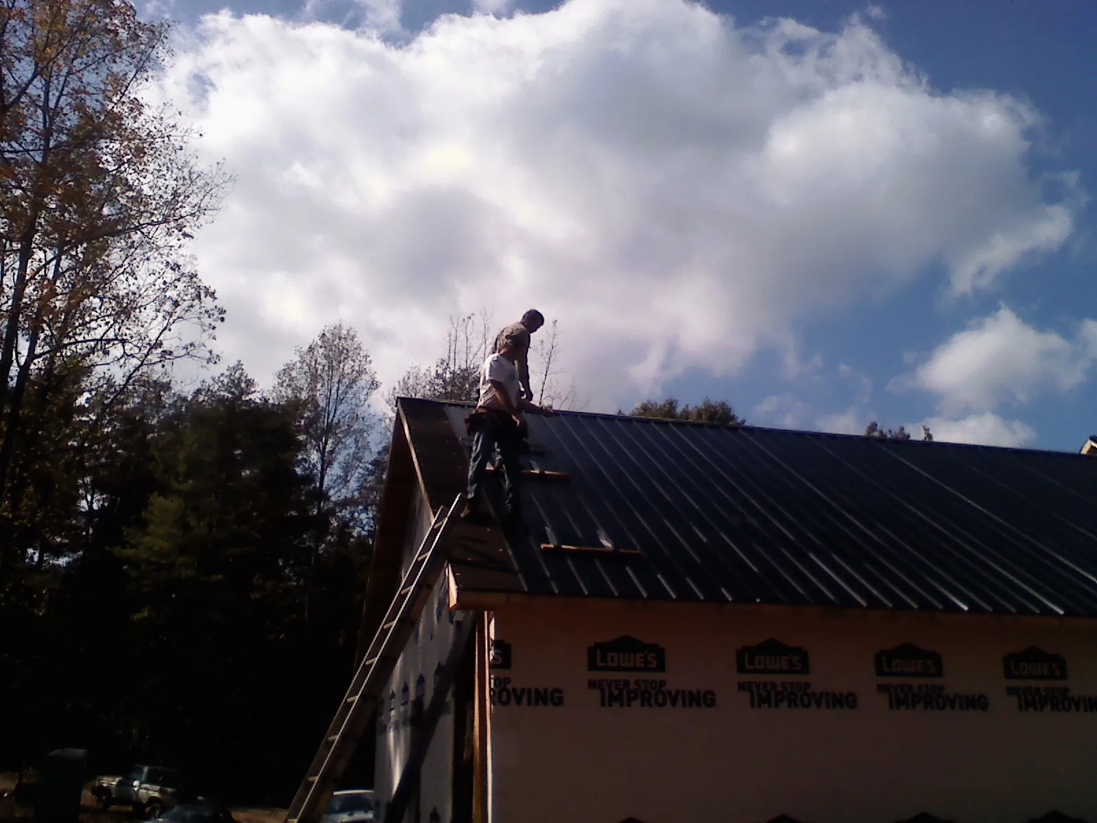 Roofer fastening dark metal panels high against a cloudy sky, from a Roof Inspection job in Universal City